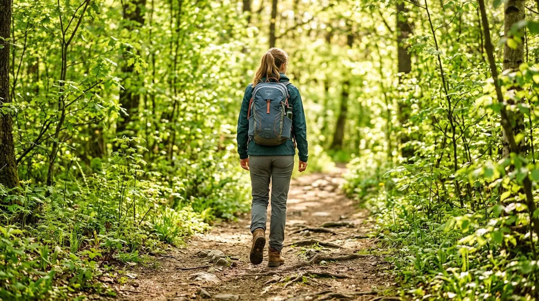 Frau von hinten auf einem Waldweg im Frühling – Wandern mit Rucksack und Trekkingschuhen im grünen Wald