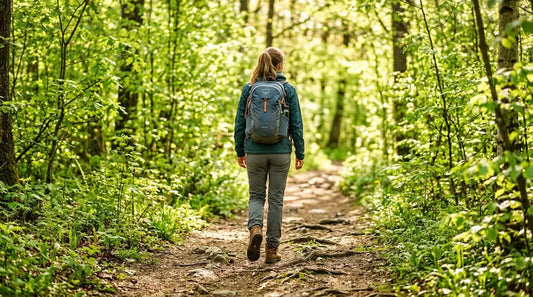 Frau von hinten auf einem Waldweg im Frühling – Wandern mit Rucksack und Trekkingschuhen im grünen Wald