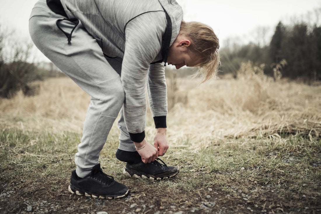 Junger Mann bindet seine Wanderschuhe auf einem Naturweg – Symbolbild für Fußschmerzen beim Gehen durch ungeeignetes Schuhwerk.