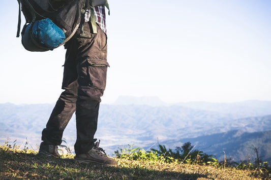 Wanderer mit Rucksack steht auf einem Bergpfad mit Blick auf eine weite Berglandschaft beim Outdoor-Wandern