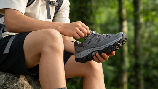 Person sitzt auf einem Felsen im Wald und hält einen Wanderschuh in den Händen – Sohle und Profil eines Trekkingschuhs im Detail